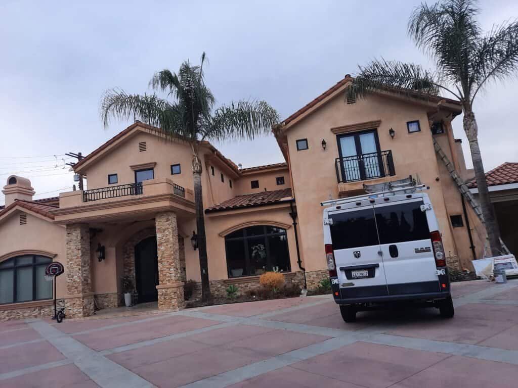 Premium exterior house painting in California by AAF Painting Inc, showcasing a beautifully painted Mediterranean-style home with warm-toned stucco walls, stone accents, and lush palm trees.