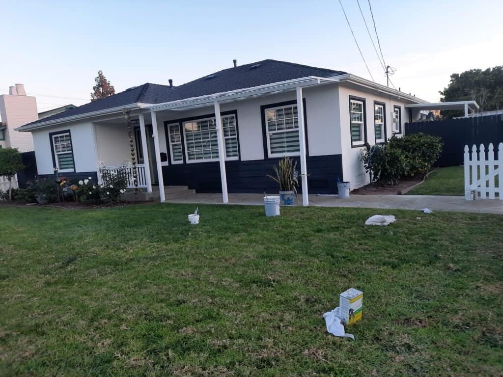 Bright white house with navy blue trim, freshly painted exterior, surrounded by green lawn and landscaped garden, showcasing professional residential painting services by AAF Painting Inc.