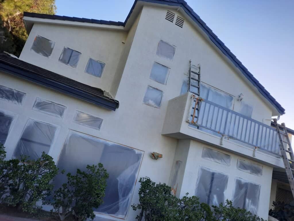 Crane painting house exterior, painter working on home renovation, professional house painting services, residential paint job on modern home, house painting with scaffolding and ladders.