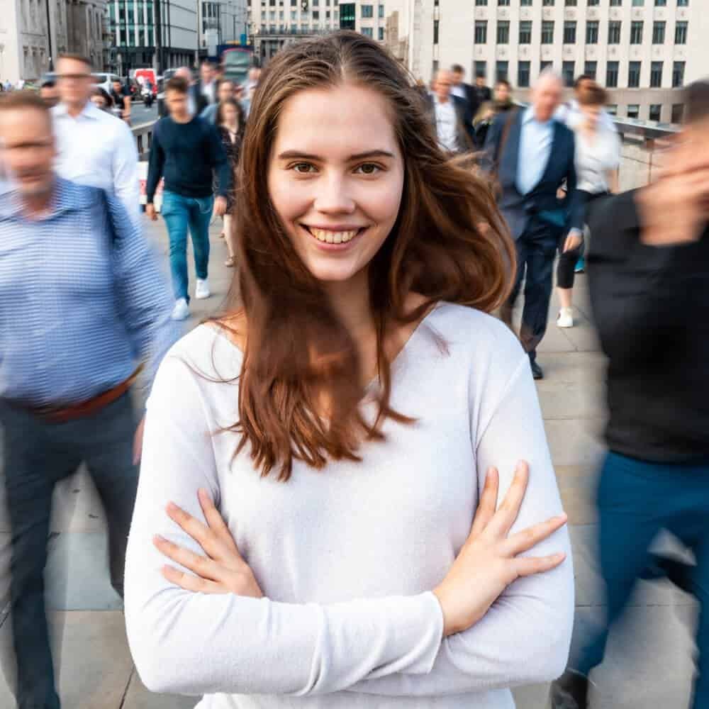 Healthy young woman smiling in a business district with blurred professional crowd, emphasizing urban lifestyle.
