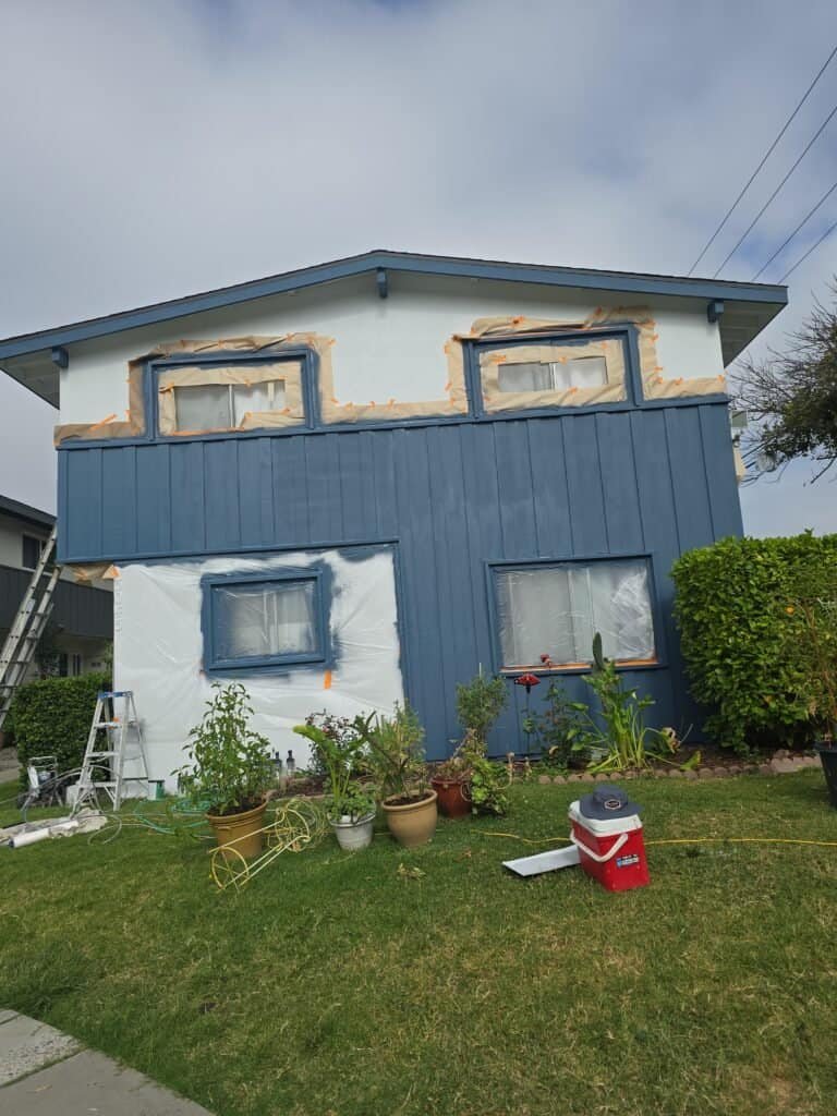 Bright blue exterior house painting in progress, showcasing professional painting services for residential homes. Skilled painters are applying fresh coats of paint to enhance curb appeal and protect the structure.