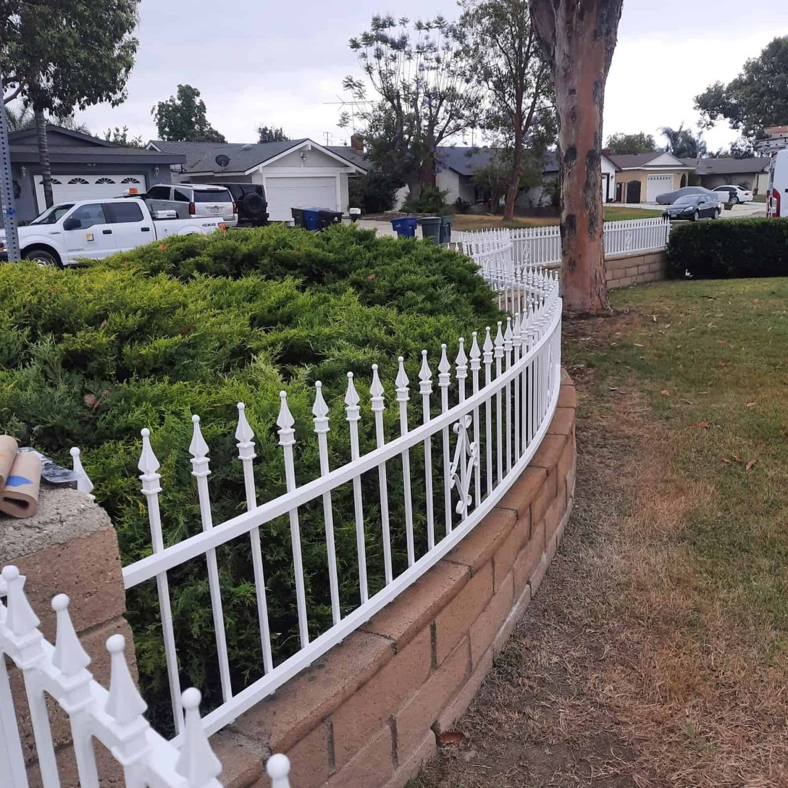 Versatile white ornamental garden fence with decorative finials, installed along a landscaped yard with brick foundation and lush greenery, showcasing professional outdoor fencing installation by AAF Painting Inc.