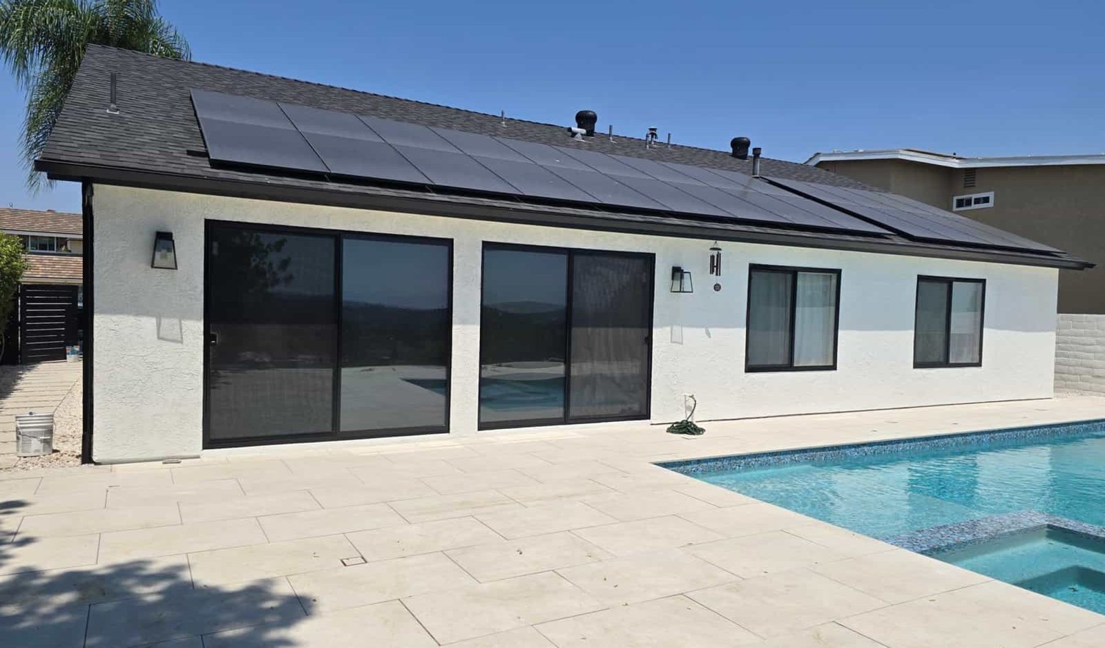 Solar panel installation on a modern house exterior, showcasing eco-friendly energy solutions, with a swimming pool and outdoor patio, emphasizing professional residential solar and painting services.