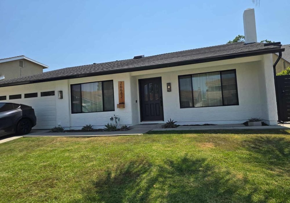 Bright white house with black doors and window frames, featuring a well-maintained lawn and modern exterior painting by AAF Painting Inc. Expert residential and commercial painting services.