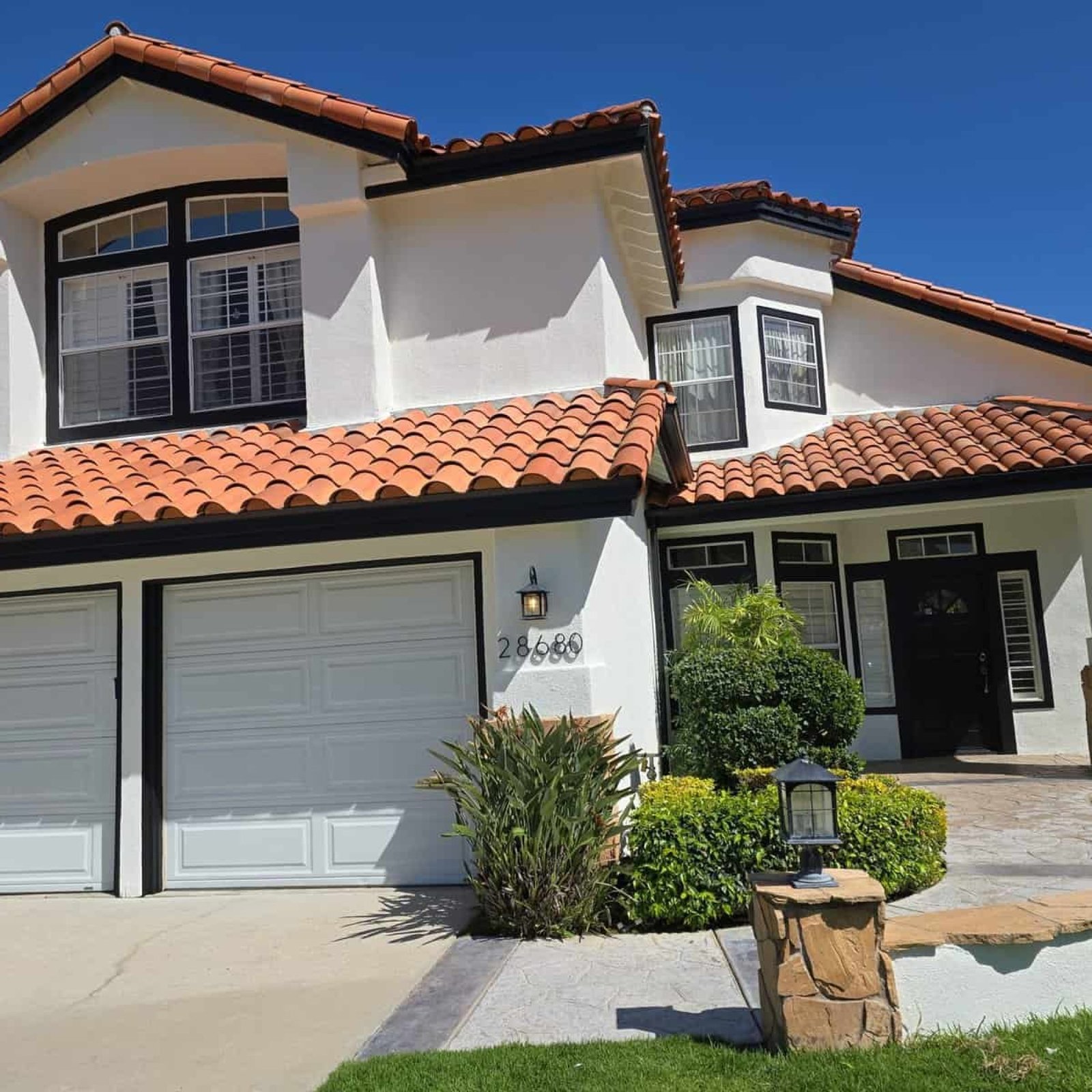 Vivid exterior house painting with a clean white finish, red clay tile roof, and black trim, showcasing professional residential painting services by AAF Painting Inc. in a sunny neighborhood.